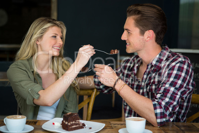 Smiling couple feeding each other dessert in cafe