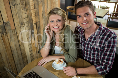 Happy young couple with coffee and laptop in cafe