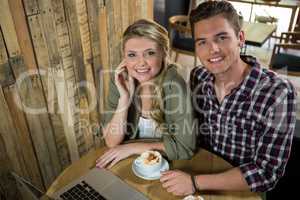 Happy young couple with coffee and laptop in cafe