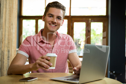Portrait of smiling man using laptop while having coffee in cafe
