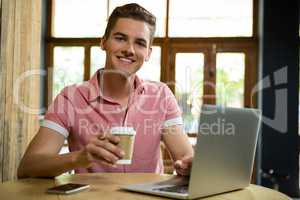 Portrait of smiling man using laptop while having coffee in cafe