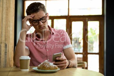 Tensed man using smart phone in coffee shop