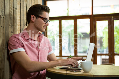 Handsome young man using laptop at table in coffee shop