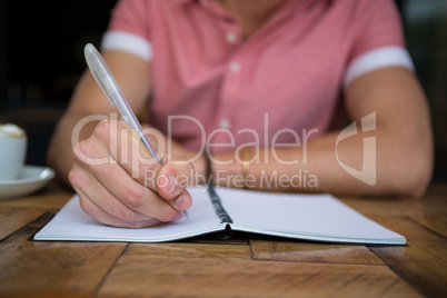 Man writing in diary at table in coffee shop
