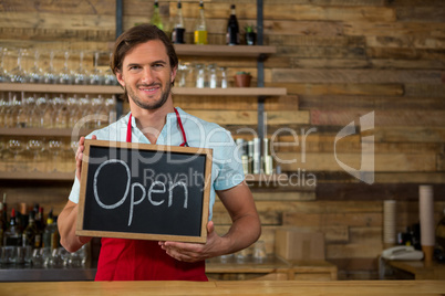 Happy barista holding open signboard in coffee shop