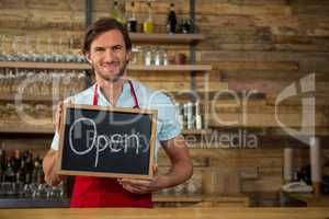 Happy barista holding open signboard in coffee shop