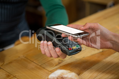 Barista accepting payment through smart phone in coffee shop