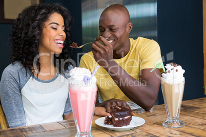 Man feeding dessert to woman in coffee shop