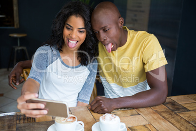 Couple making faces while taking selfie in coffee shop