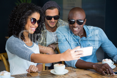 Friends wearing sunglasses while taking selfie in coffee shop