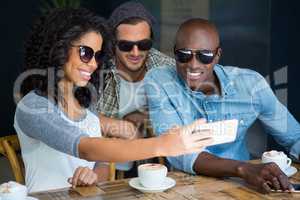Friends wearing sunglasses while taking selfie in coffee shop
