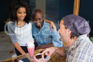 Man showing mobile phone to couple at table in coffee shop