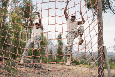 Military soldiers climbing a net during obstacle course