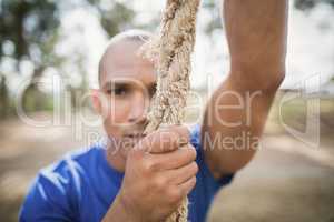 Portrait of fit man climbing rope during obstacle course