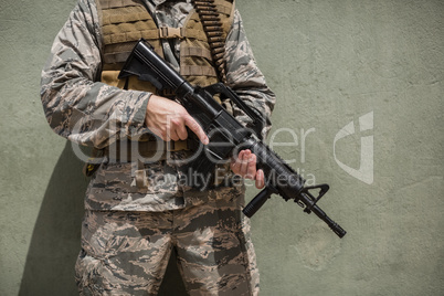 Mid section of military soldier standing with a rifle against concrete wall