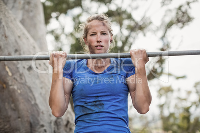 Fit woman performing pull-ups on bar during obstacle course