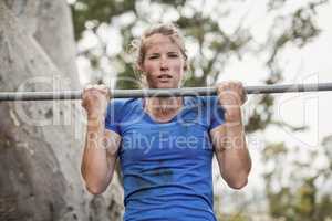 Fit woman performing pull-ups on bar during obstacle course