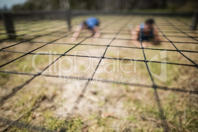 Fit man and woman crawling under the net during obstacle course