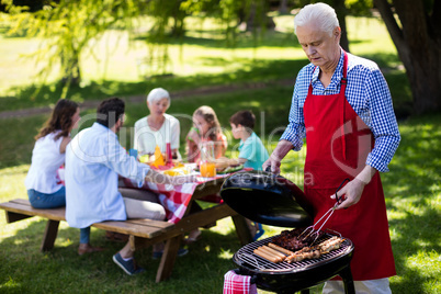 Senior man barbequing with family in background