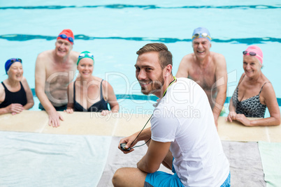 Cheerful male instructor assisting senior swimmers