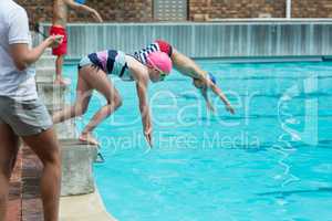 Female instructor monitoring time of children diving in pool