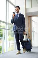 Businessman with trolley bag using mobile phone