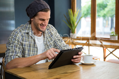 Smiling man using tablet computer at table in coffee house
