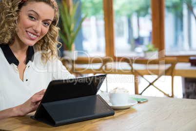 Smiling young woman using digital table at table in coffee shop