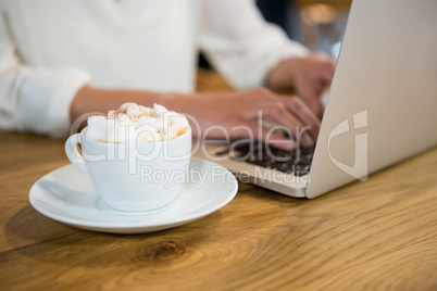 Woman using laptop by coffee with froth on table in cafe