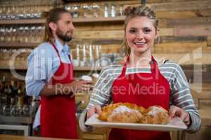 Portrait of smiling female barista holding tray of croissants in cafe