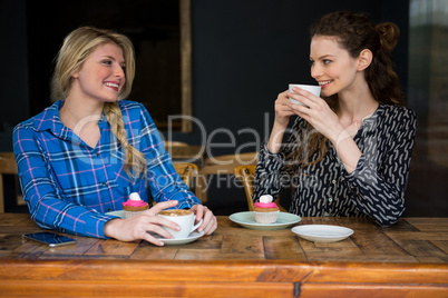 Smiling female friends having coffee while talking in cafeteria