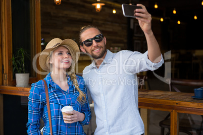 Smiling couple taking selfie with mobile phone in coffee shop