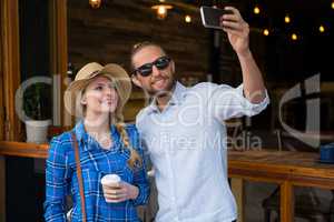 Smiling couple taking selfie with mobile phone in coffee shop