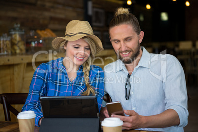 Smiling couple using mobile phone at table in cafe