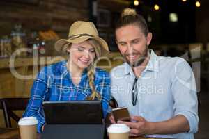 Smiling couple using mobile phone at table in cafe