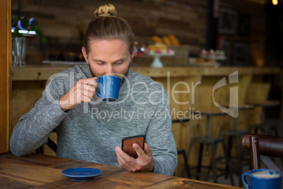 Man drinking coffee while using smart phone in cafe