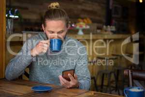 Man drinking coffee while using smart phone in cafe