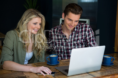 Smiling couple using laptop at table in cafeteria