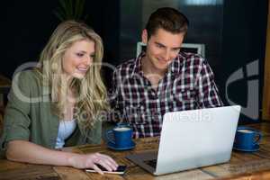 Smiling couple using laptop at table in cafeteria