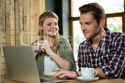 Woman looking at man using laptop in coffee shop