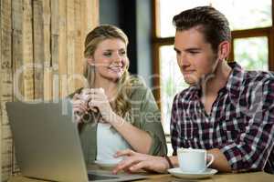 Woman looking at man using laptop in coffee shop