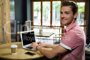 Smiling young man using laptop at table in coffee shop