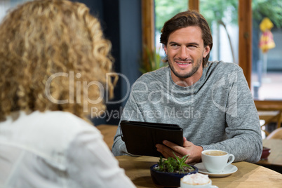 Man holding tablet PC while looking at woman in coffee shop