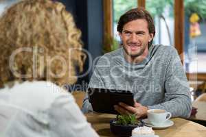Man holding tablet PC while looking at woman in coffee shop