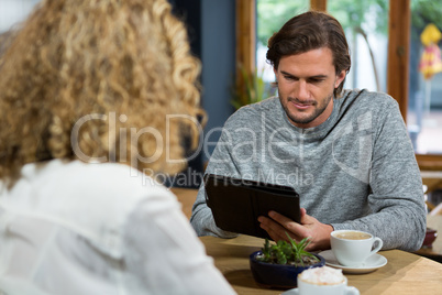 Man using digital tablet with woman in foreground at coffee house