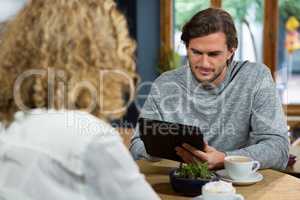 Man using digital tablet with woman in foreground at coffee house