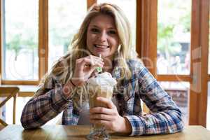 Smiling young woman drinking milkshake with straw in cafe
