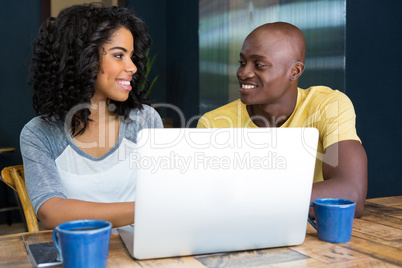 Couple looking at each other with laptop on table in coffee shop