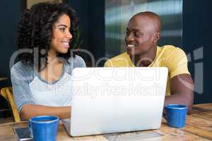 Couple looking at each other with laptop on table in coffee shop