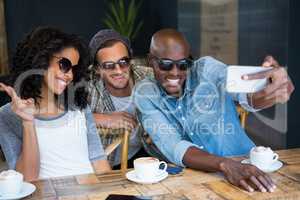 Cheerful friends wearing sunglasses while taking selfie in coffee shop